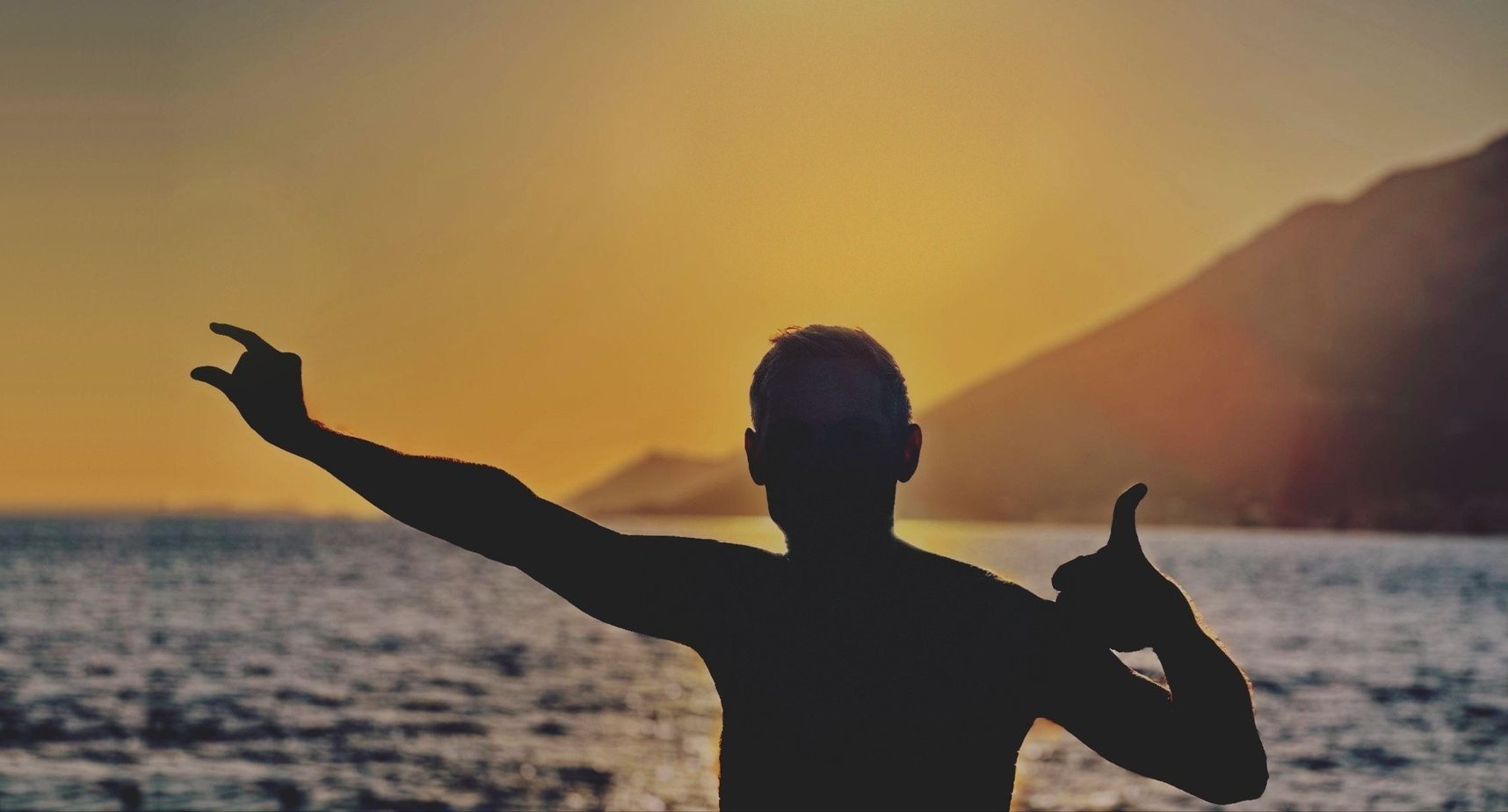 Blaz Umek in silhouette at sunset over the sea, reaching for the sun between two fingers